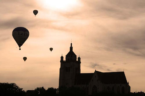 photographie de la basilique de Dole, au couch de soleil, avec des montgolfires en vol